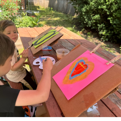two kids painting outside with cardboard easels
