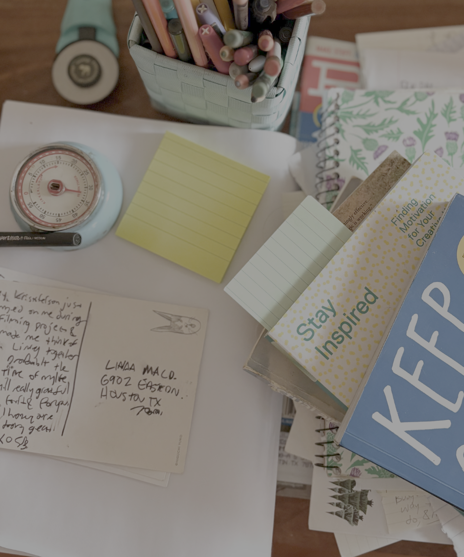 desk with a postcard, sticky note, pens and stack of books